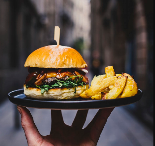 a hand holding a burger with fried potato slices on a black plate